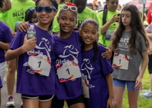 Three girls in purple shirts smile together at the start line